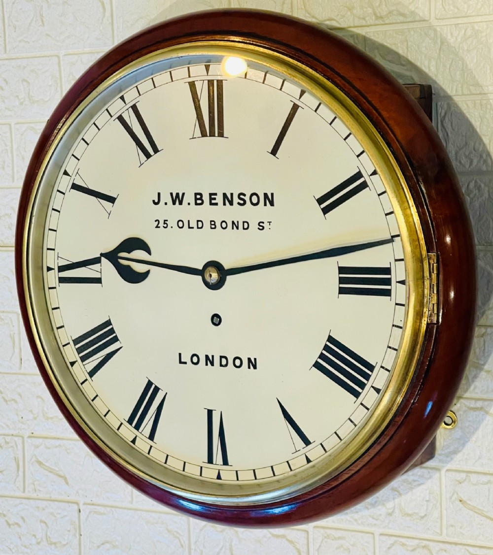 A circular mahogany fusee wall clock featuring a white dial face with black Roman numerals, brass bezel, and J. W. Benson London markings. View V