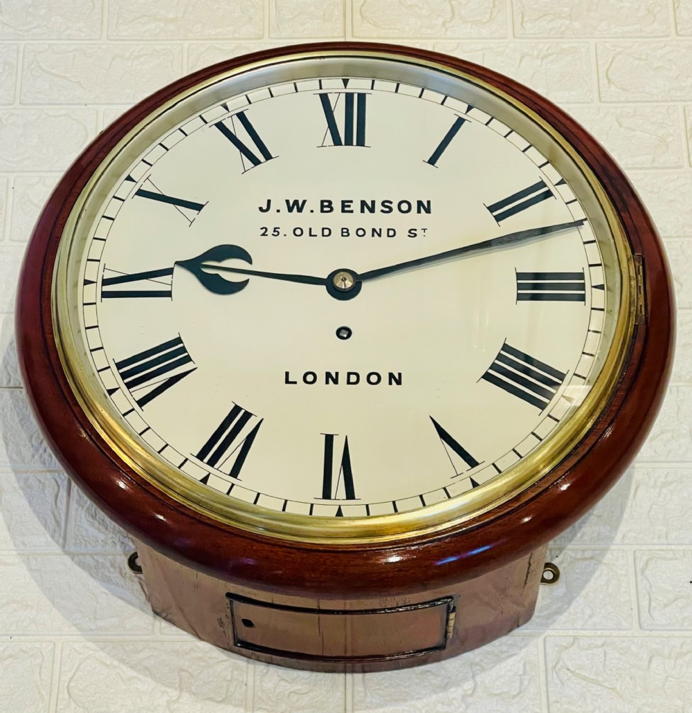 A circular mahogany fusee wall clock featuring a white dial face with black Roman numerals, brass bezel, and J. W. Benson London markings. View VII