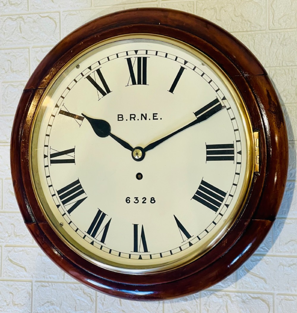 A circular Victorian railway dial clock with a dark mahogany frame, brass bezel, and off-white dial featuring black Roman numerals.