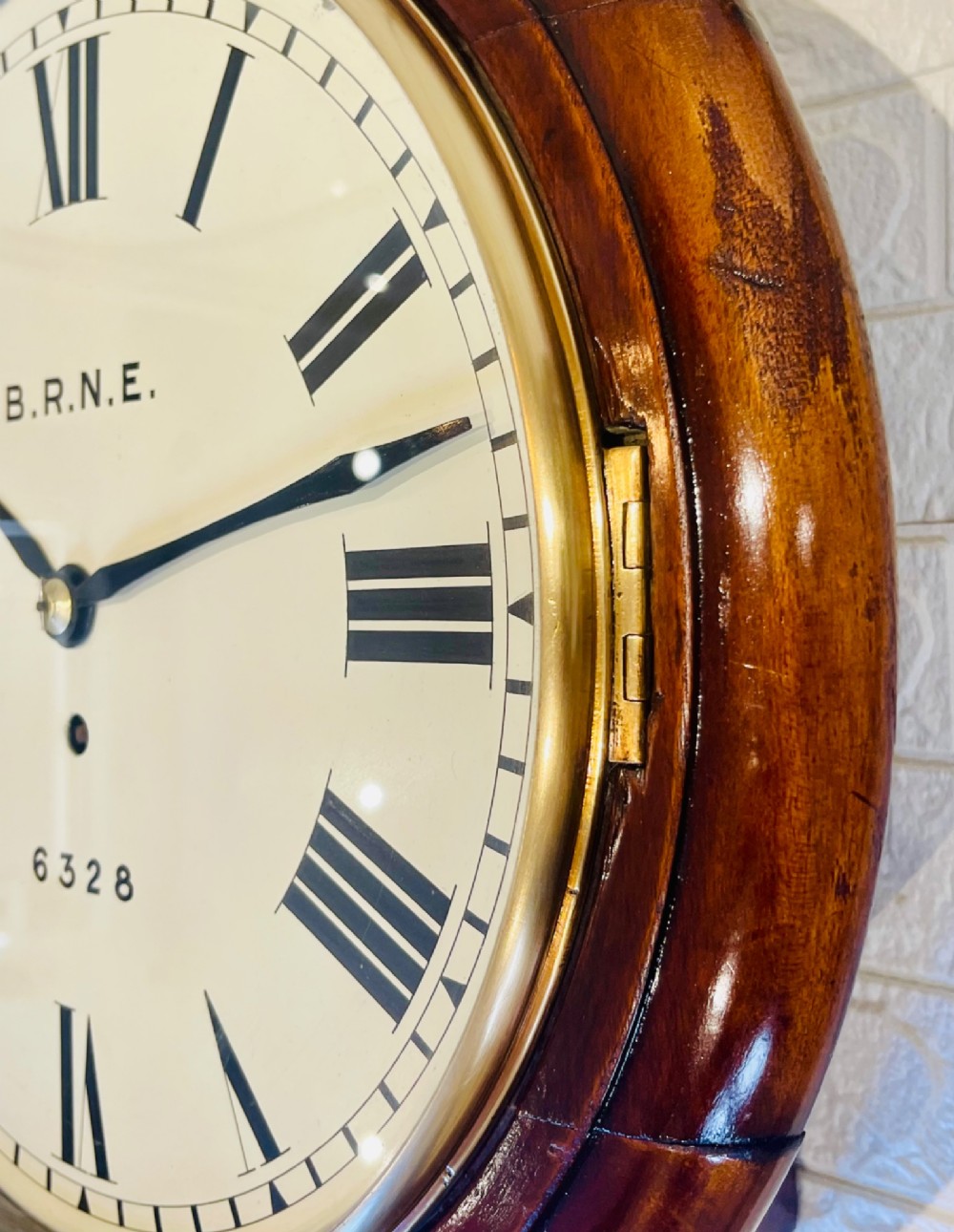 A circular Victorian railway dial clock with a dark mahogany frame, brass bezel, and off-white dial featuring black Roman numerals. View V