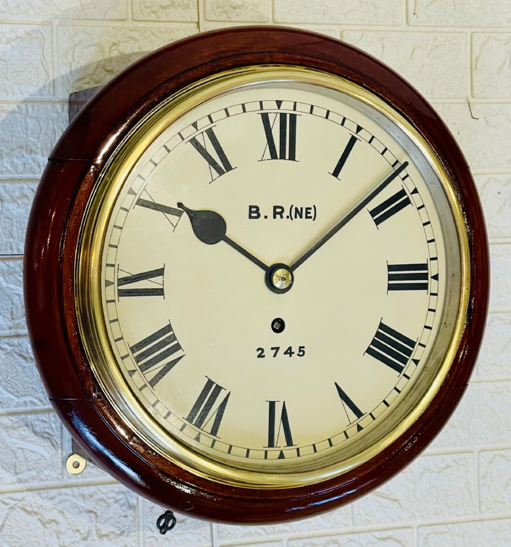 A circular 10-inch railway dial wall clock featuring a turned mahogany wooden surround, a brass bezel, and a cream dial marked B.R.(NE) with black Roman numerals.