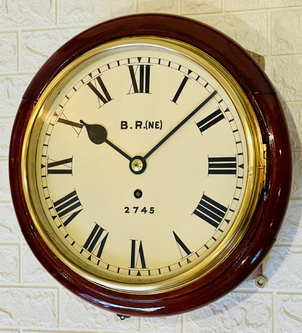 A circular 10-inch railway dial wall clock featuring a turned mahogany wooden surround, a brass bezel, and a cream dial marked B.R.(NE) with black Roman numerals. View II
