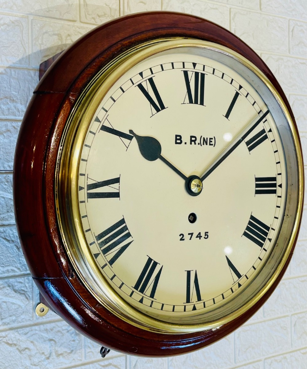 A circular 10-inch railway dial wall clock featuring a turned mahogany wooden surround, a brass bezel, and a cream dial marked B.R.(NE) with black Roman numerals. View IV