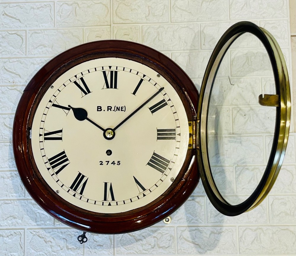 A circular 10-inch railway dial wall clock featuring a turned mahogany wooden surround, a brass bezel, and a cream dial marked B.R.(NE) with black Roman numerals. View V