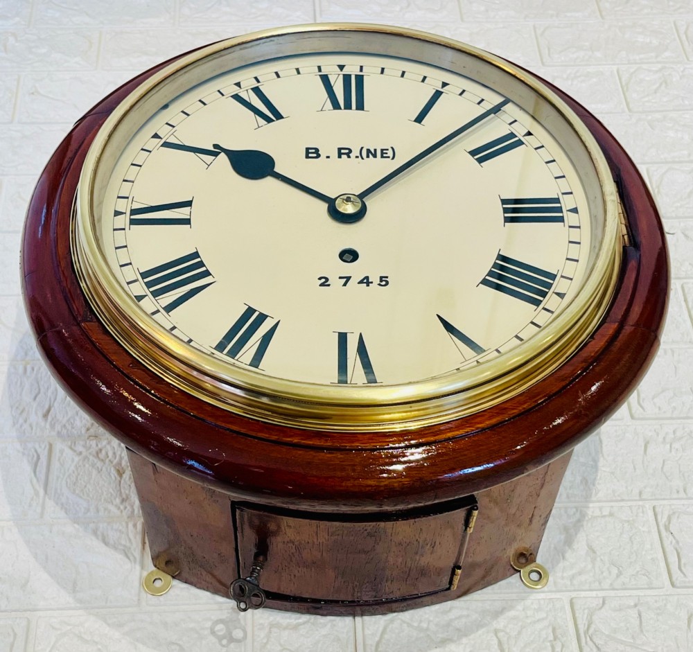 A circular 10-inch railway dial wall clock featuring a turned mahogany wooden surround, a brass bezel, and a cream dial marked B.R.(NE) with black Roman numerals. View VI
