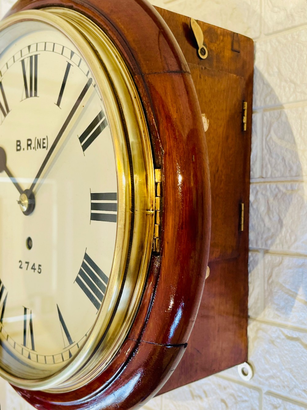 A circular 10-inch railway dial wall clock featuring a turned mahogany wooden surround, a brass bezel, and a cream dial marked B.R.(NE) with black Roman numerals. View VII