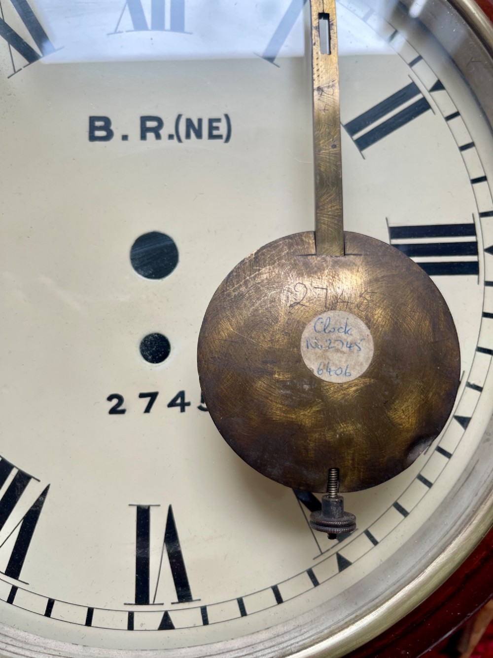 A circular 10-inch railway dial wall clock featuring a turned mahogany wooden surround, a brass bezel, and a cream dial marked B.R.(NE) with black Roman numerals. View X