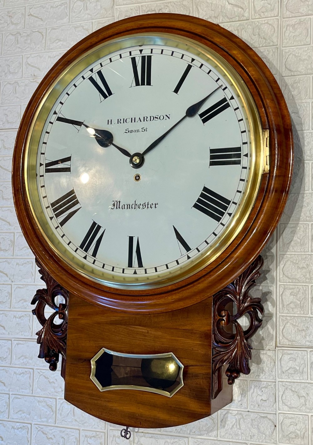 Victorian oak drop dial wall clock featuring a circular white dial with Roman numerals, a brass bezel, and carved side scrolls. View III