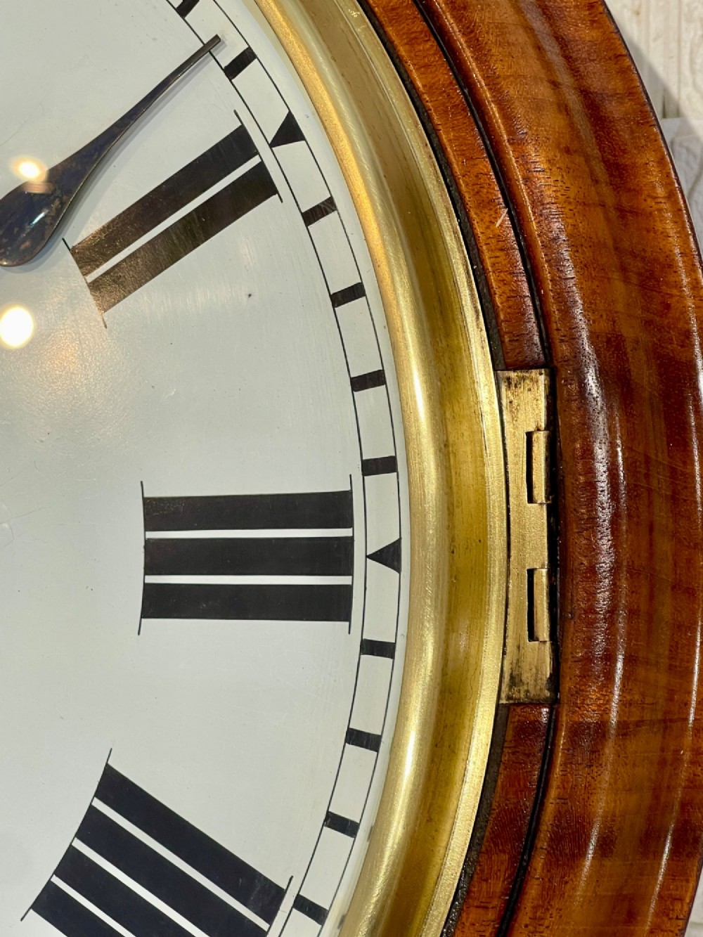 Victorian oak drop dial wall clock featuring a circular white dial with Roman numerals, a brass bezel, and carved side scrolls. View V