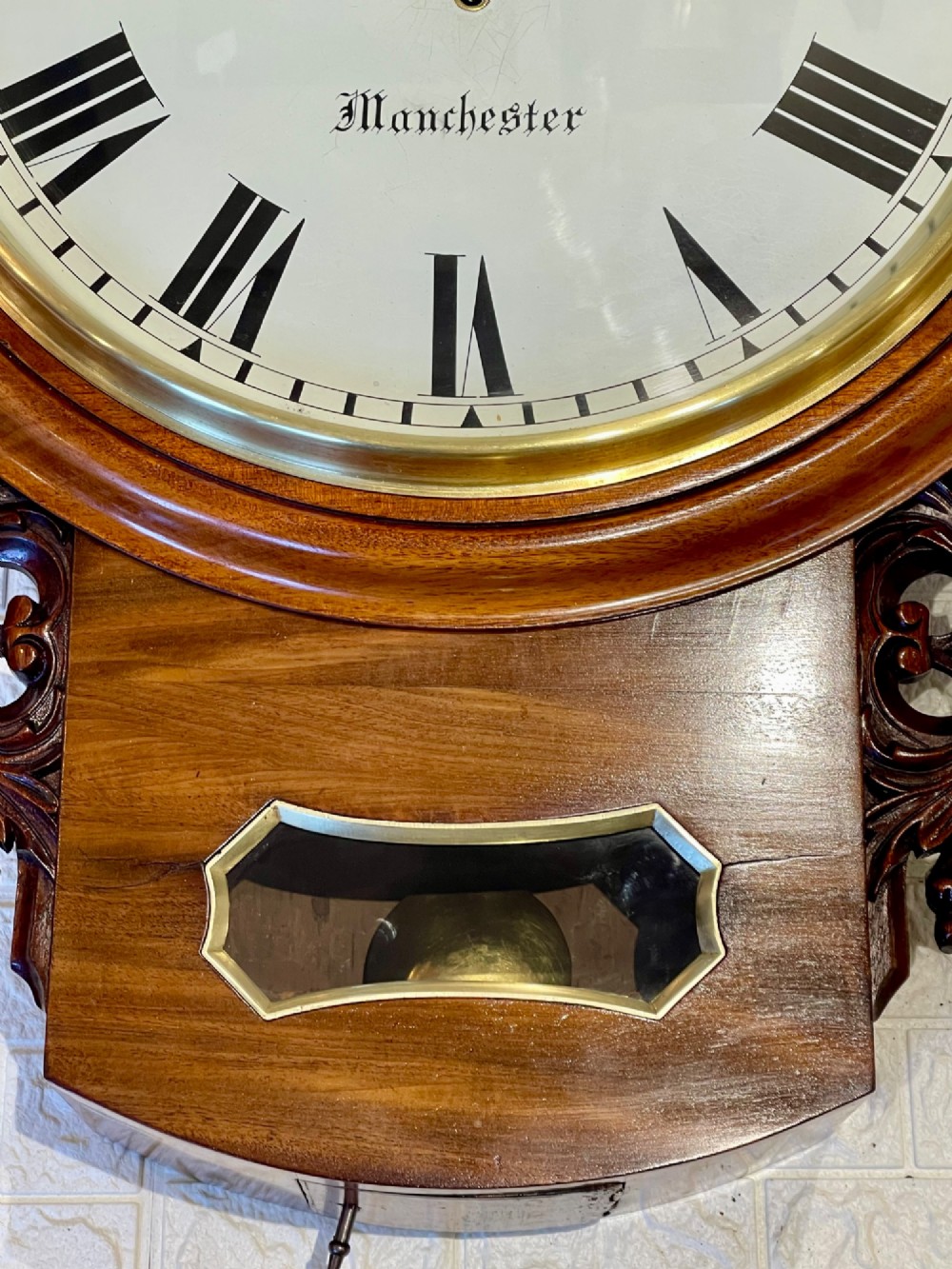 Victorian oak drop dial wall clock featuring a circular white dial with Roman numerals, a brass bezel, and carved side scrolls. View VI