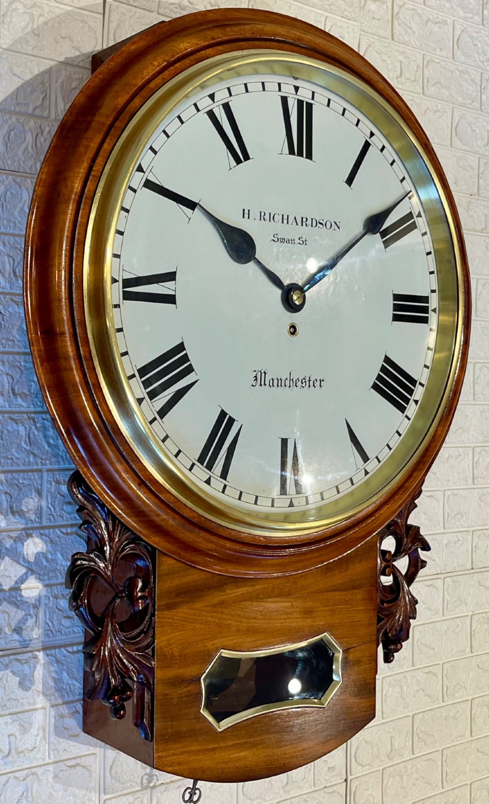 Victorian oak drop dial wall clock featuring a circular white dial with Roman numerals, a brass bezel, and carved side scrolls. View IX