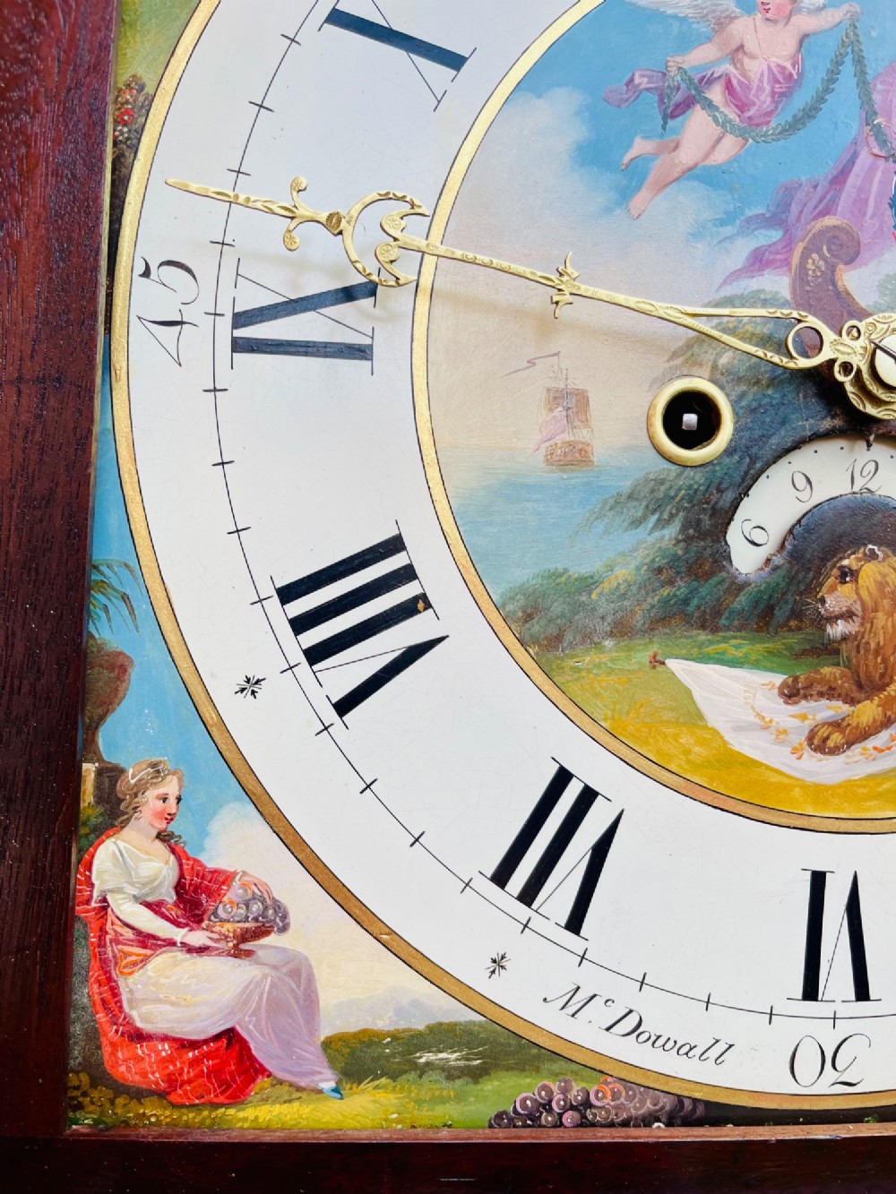 A tall Regency mahogany longcase clock featuring a swan-neck hood pediment, brass finial, fluted columns, and a hand-painted dial with figurative scenes. View XI