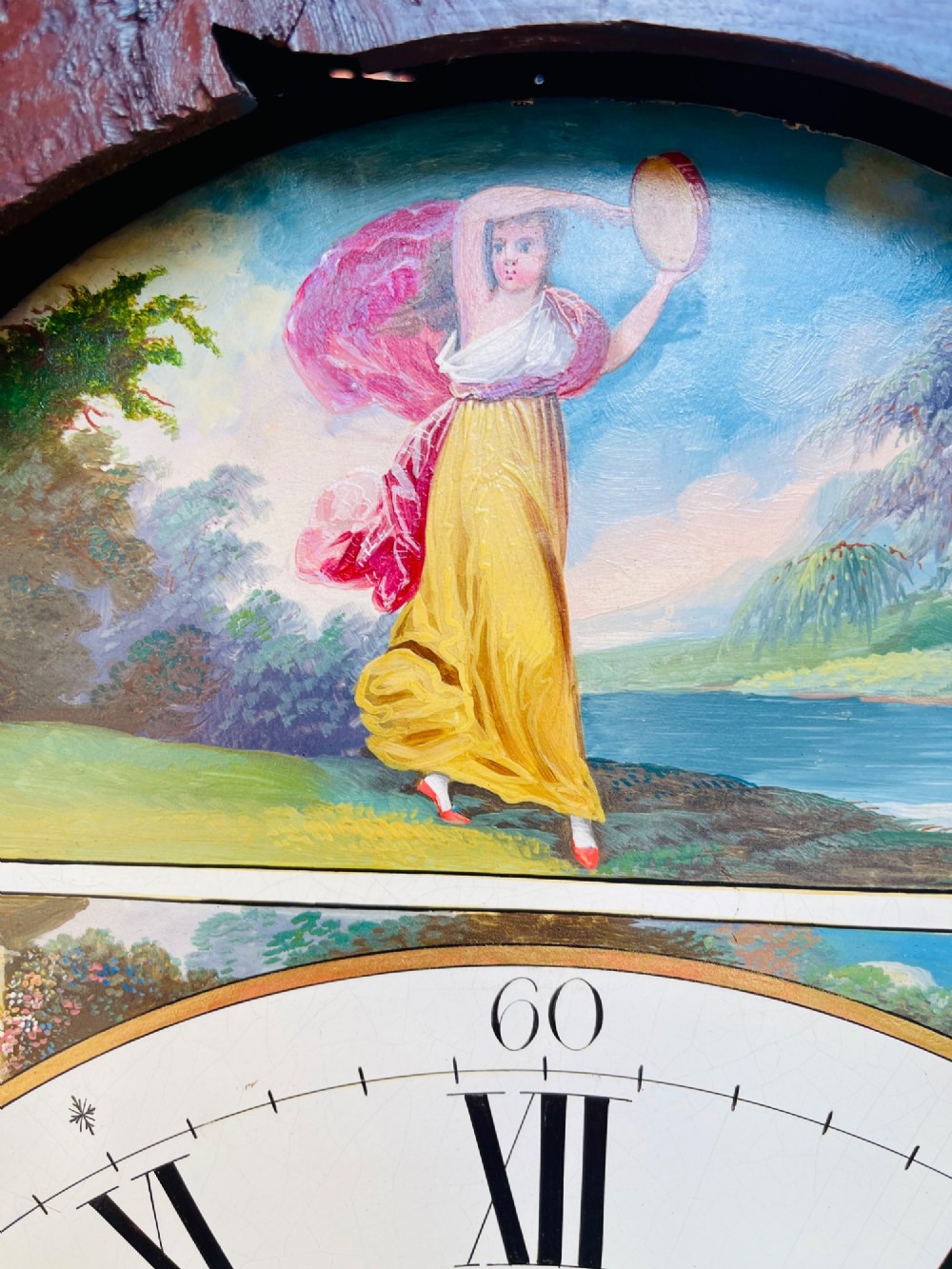 A tall Regency mahogany longcase clock featuring a swan-neck hood pediment, brass finial, fluted columns, and a hand-painted dial with figurative scenes. View XV