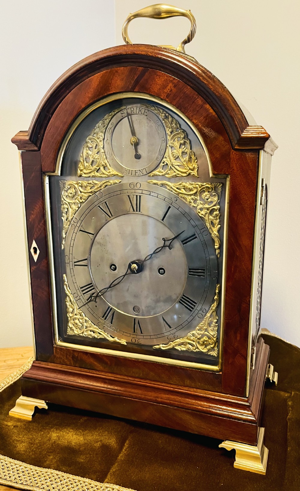 A George III mahogany bracket clock featuring an arched case with a brass top handle, gilt spandrels, and a silvered dial.