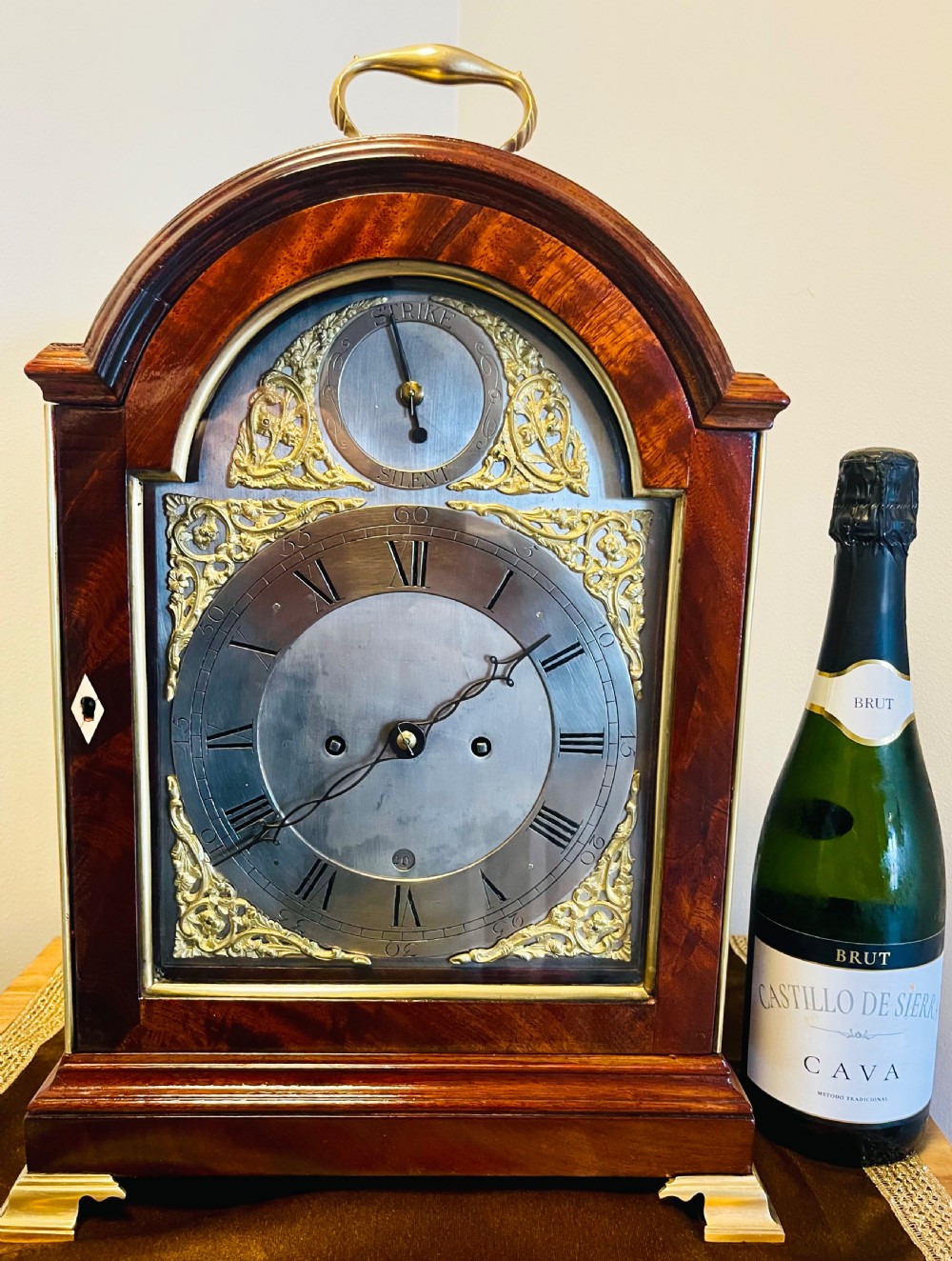 A George III mahogany bracket clock featuring an arched case with a brass top handle, gilt spandrels, and a silvered dial. View X