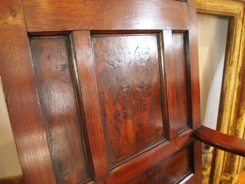 fig 2. An eighteenth-century dark oak wainscot armchair featuring a panelled backrest, carved finials, turned front legs, and sturdy wooden stretchers.
