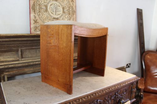 fig 1. An oak stool featuring solid slab side supports, a central connecting stretcher, and a concave upholstered fabric seat cushion.