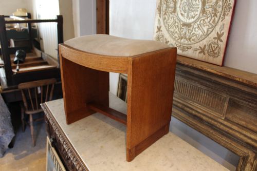 fig 2. An oak stool featuring solid slab side supports, a central connecting stretcher, and a concave upholstered fabric seat cushion.