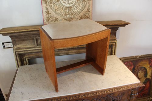 fig 3. An oak stool featuring solid slab side supports, a central connecting stretcher, and a concave upholstered fabric seat cushion.