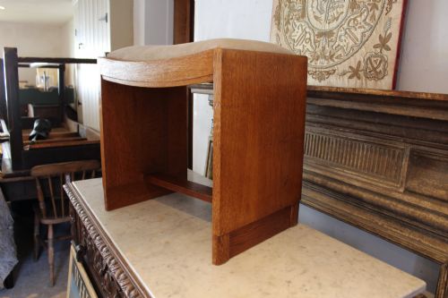 fig 5. An oak stool featuring solid slab side supports, a central connecting stretcher, and a concave upholstered fabric seat cushion.