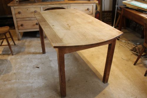 fig 3. An Edwardian light oak dining table featuring a rectangular top with subtly curved short ends, supported by four straight square legs.