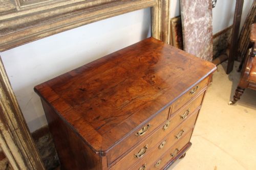 fig 3. A compact George II walnut chest of drawers featuring decorative brass handles, crossbanded veneer top, and turned bun feet.