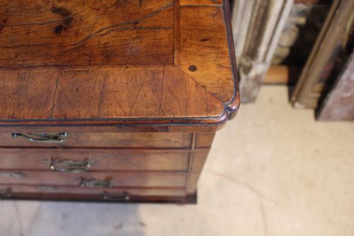 fig 6. A compact George II walnut chest of drawers featuring decorative brass handles, crossbanded veneer top, and turned bun feet.