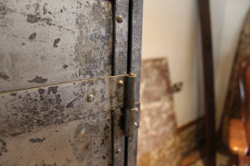 fig 2. A tall, narrow Victorian industrial metal cupboard featuring a single door with a dark grey patinated surface, riveted frame, brass number plaque, and latch handle.
