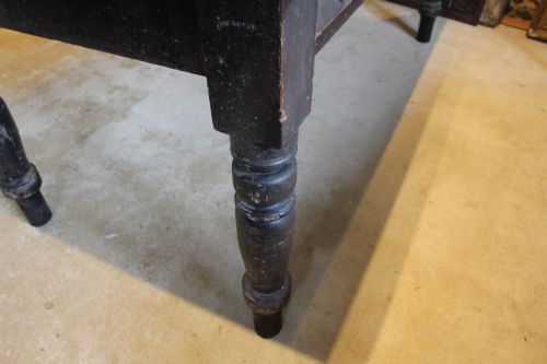 fig 5. A 19th-century pine farmhouse dining table featuring a natural scrubbed wooden top, frieze drawers with round wooden knobs, and turned dark painted legs.
