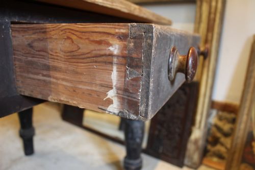 fig 7. A 19th-century pine farmhouse dining table featuring a natural scrubbed wooden top, frieze drawers with round wooden knobs, and turned dark painted legs.