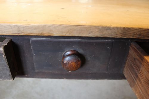 fig 8. A 19th-century pine farmhouse dining table featuring a natural scrubbed wooden top, frieze drawers with round wooden knobs, and turned dark painted legs.