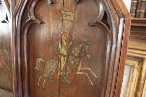 fig 2. A pair of arched dark oak architectural panels featuring carved Gothic tracery and polychrome paintings of mounted medieval knights and heraldic shields.