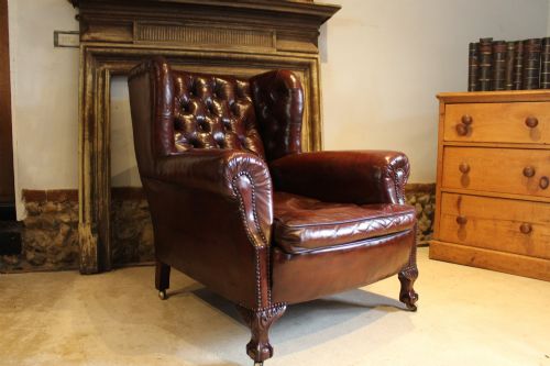fig 2. A late Victorian deep-buttoned chestnut brown leather wingback armchair featuring brass studding, carved front legs with ball-and-claw feet, and metal castors.