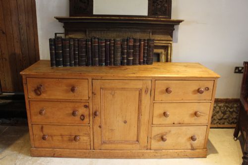 fig 1. An early Victorian honey pine dresser base featuring a central panelled cupboard door flanked by three drawers on each side with turned wooden knobs.