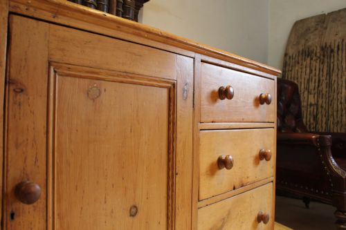 fig 2. An early Victorian honey pine dresser base featuring a central panelled cupboard door flanked by three drawers on each side with turned wooden knobs.
