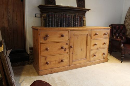 fig 7. An early Victorian honey pine dresser base featuring a central panelled cupboard door flanked by three drawers on each side with turned wooden knobs.