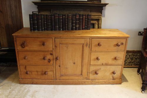 fig 9. An early Victorian honey pine dresser base featuring a central panelled cupboard door flanked by three drawers on each side with turned wooden knobs.