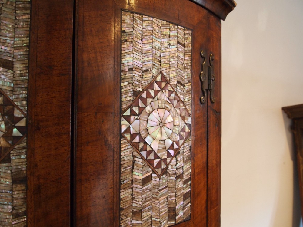 A dark walnut bowfront corner cabinet featuring two doors detailed with geometric mother of pearl inlay and brass hinges. View II
