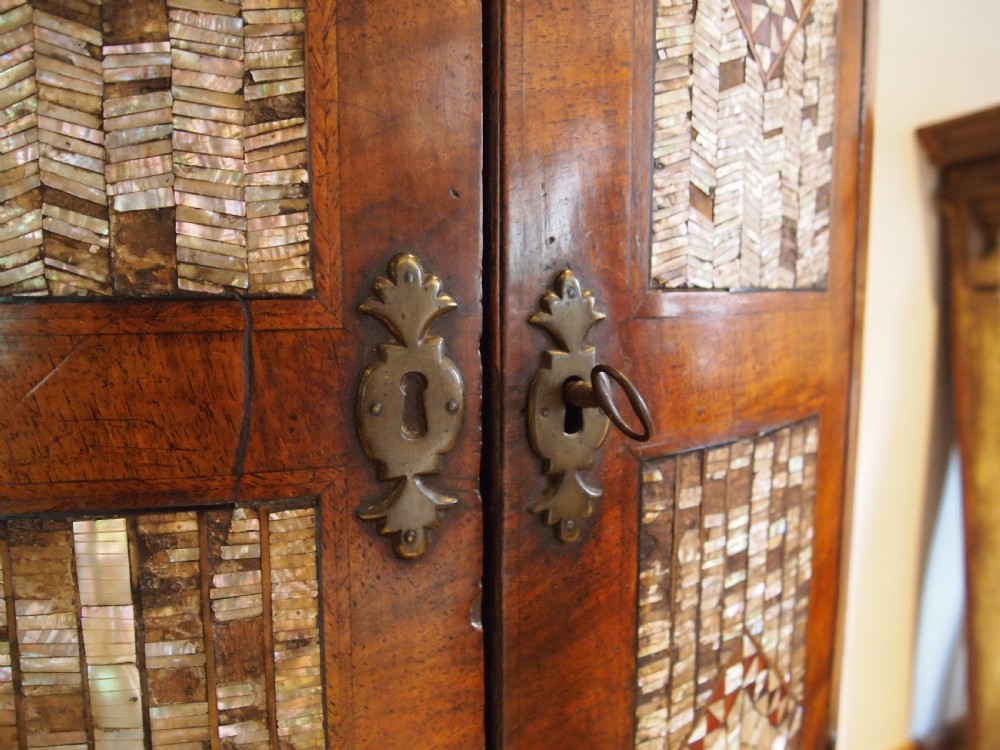 A dark walnut bowfront corner cabinet featuring two doors detailed with geometric mother of pearl inlay and brass hinges. View III