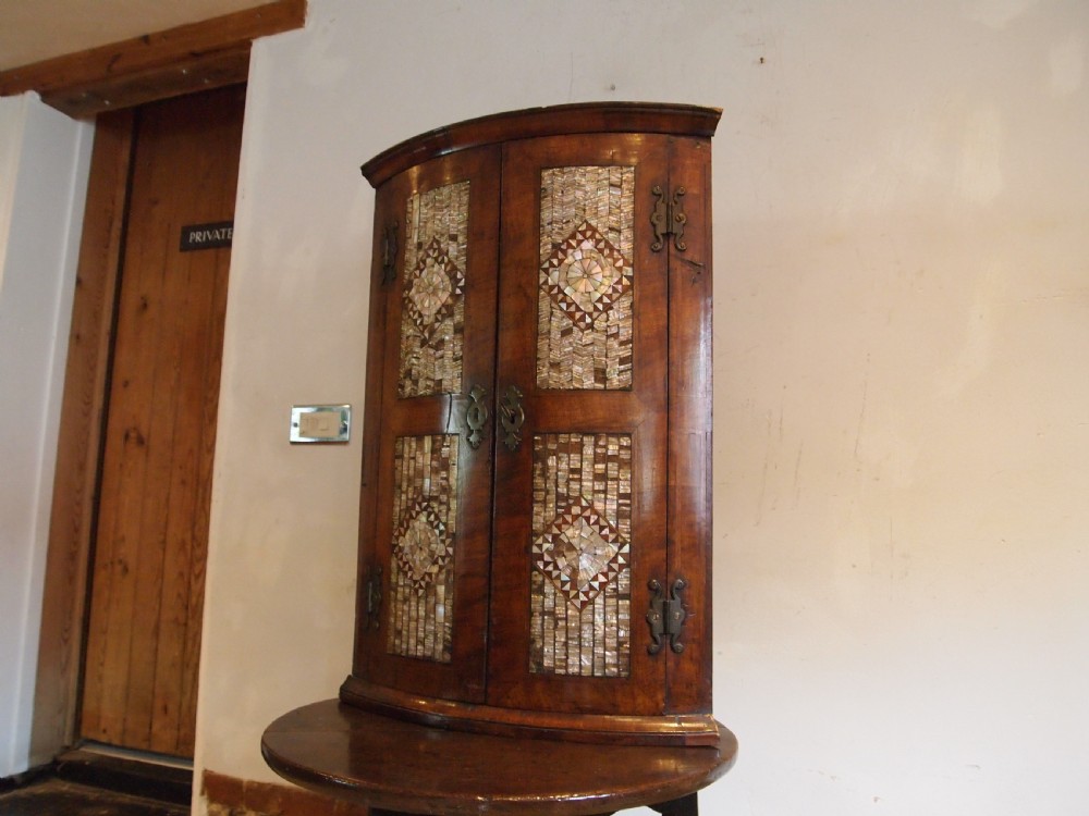 A dark walnut bowfront corner cabinet featuring two doors detailed with geometric mother of pearl inlay and brass hinges. View VII