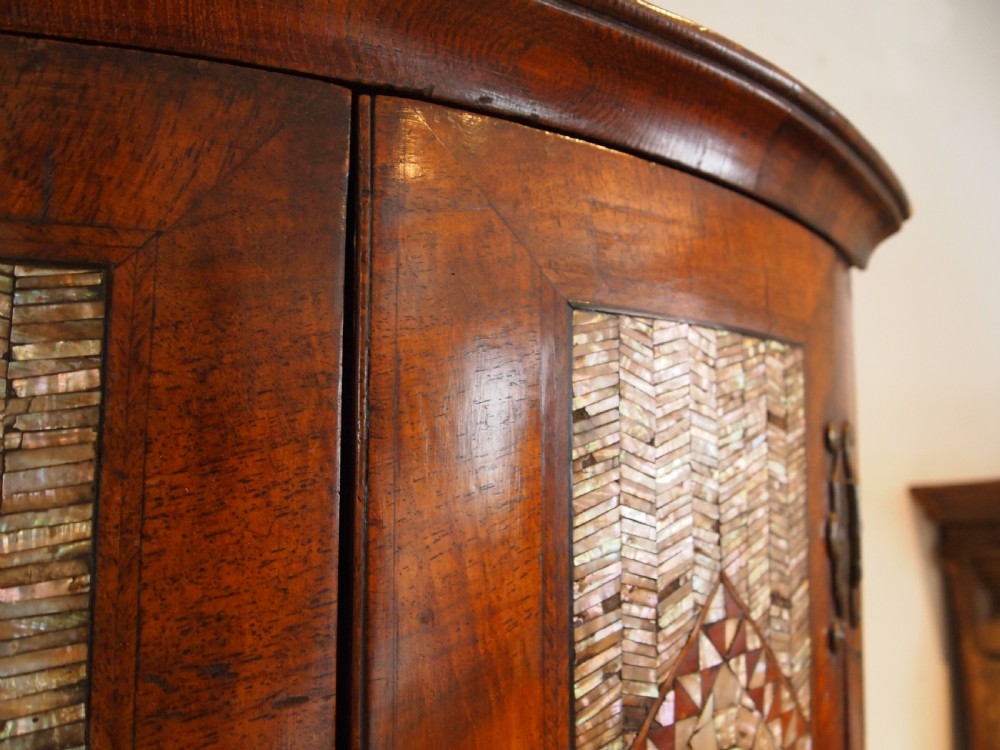 A dark walnut bowfront corner cabinet featuring two doors detailed with geometric mother of pearl inlay and brass hinges. View IX