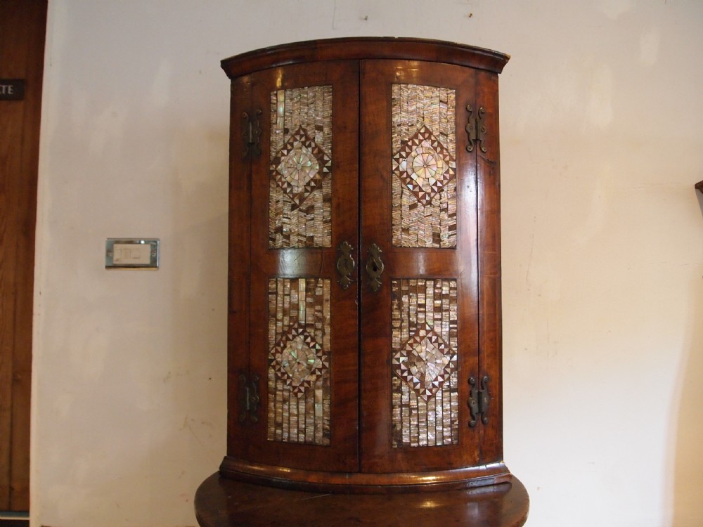 A dark walnut bowfront corner cabinet featuring two doors detailed with geometric mother of pearl inlay and brass hinges. View XI