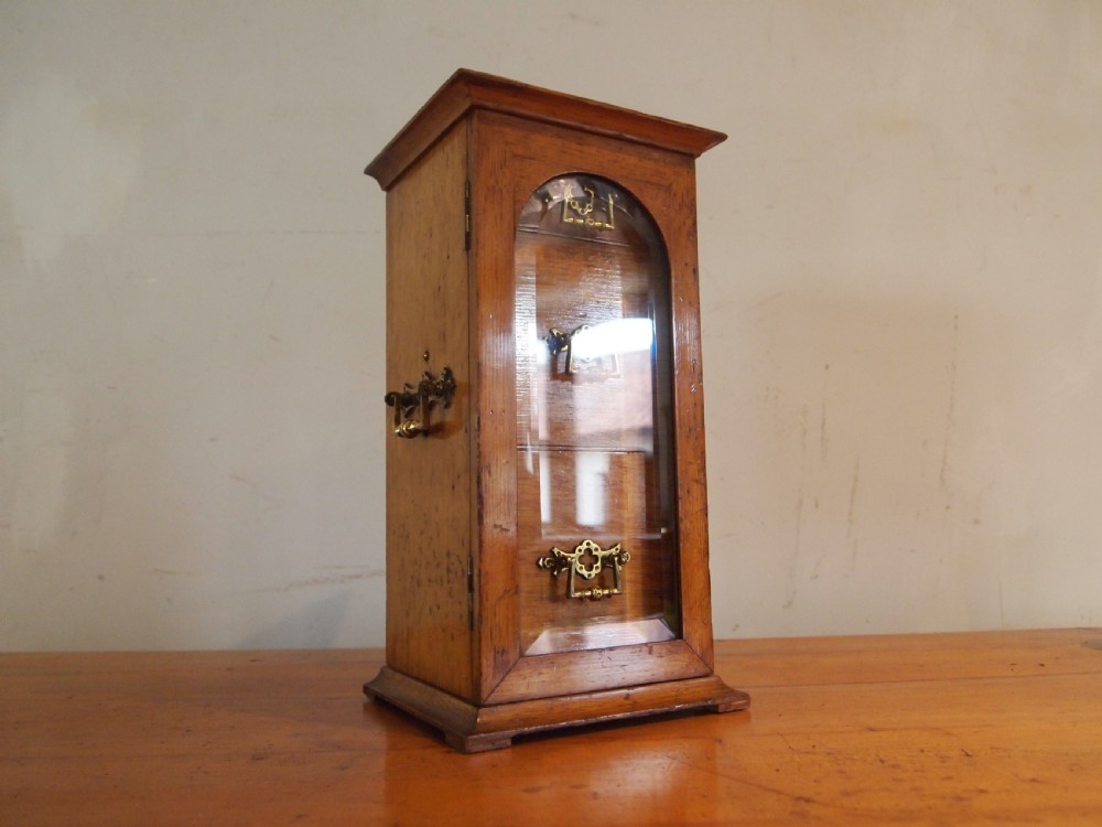 A tall Victorian oak collectors chest with an arched glass door enclosing internal drawers fitted with brass handles.