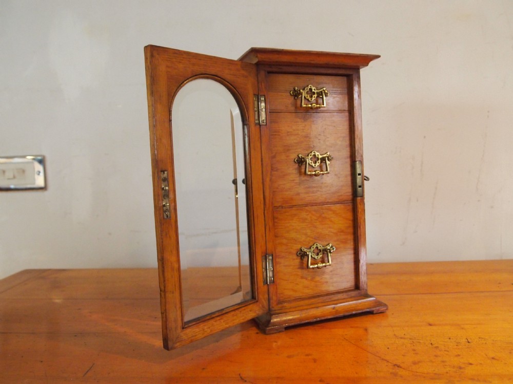 A tall Victorian oak collectors chest with an arched glass door enclosing internal drawers fitted with brass handles. View II