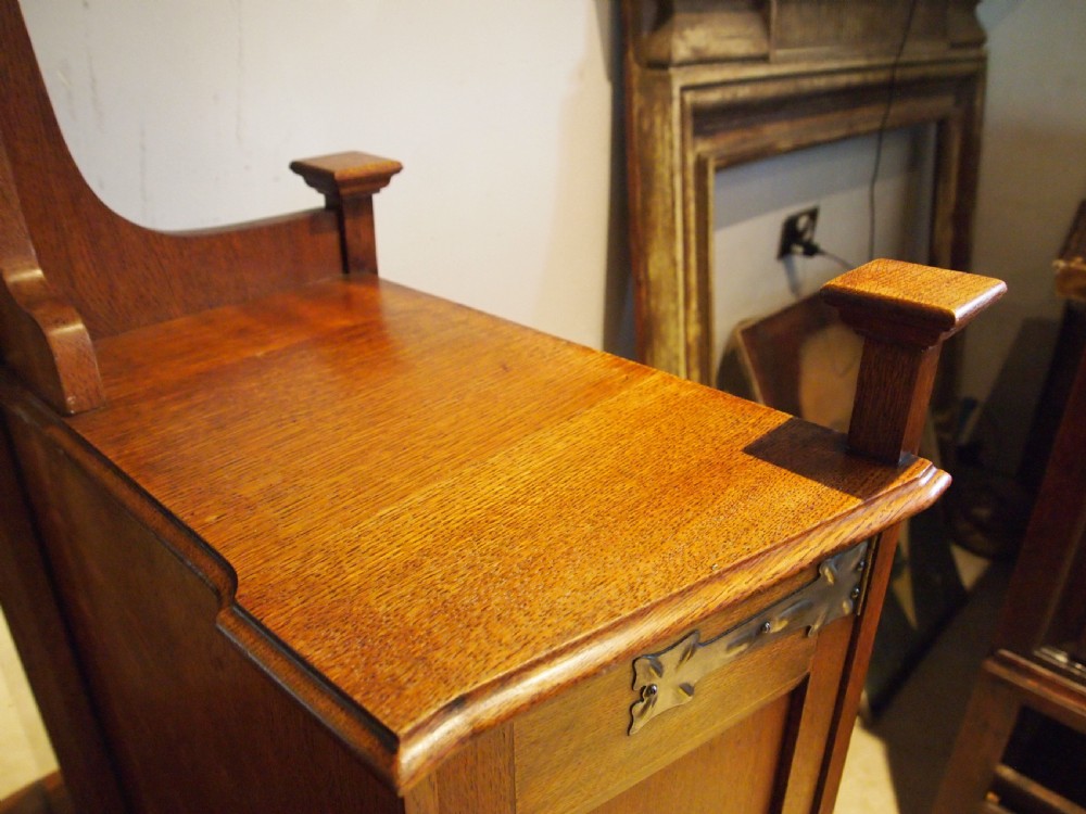 An Arts and Crafts solid oak dressing table featuring a central tall mirror flanked by two side cupboards with decorative inlaid landscape panels and metal strap hinges. View III