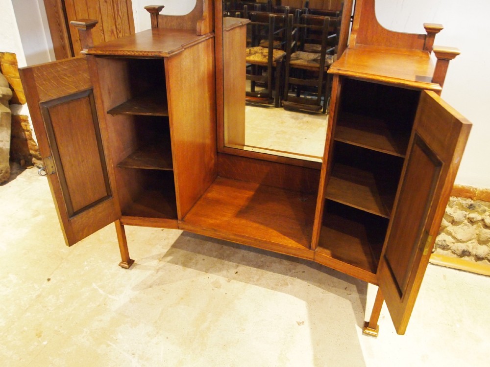 An Arts and Crafts solid oak dressing table featuring a central tall mirror flanked by two side cupboards with decorative inlaid landscape panels and metal strap hinges. View VII