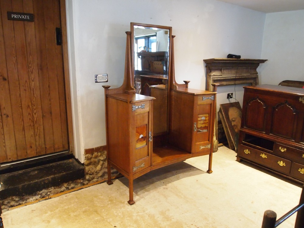 An Arts and Crafts solid oak dressing table featuring a central tall mirror flanked by two side cupboards with decorative inlaid landscape panels and metal strap hinges. View XIV