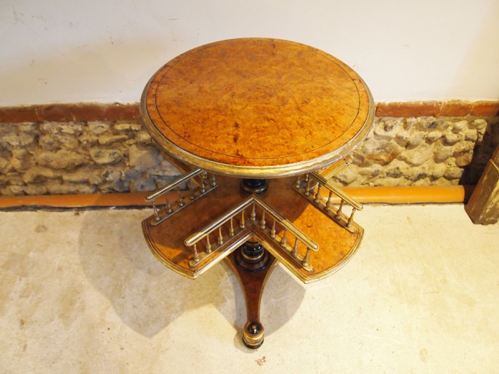 A circular Victorian burr walnut revolving library table featuring parcel gilt detailing, a turned pedestal base, and lower gallery shelves.