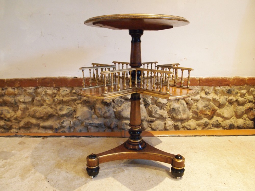 A circular Victorian burr walnut revolving library table featuring parcel gilt detailing, a turned pedestal base, and lower gallery shelves. View V