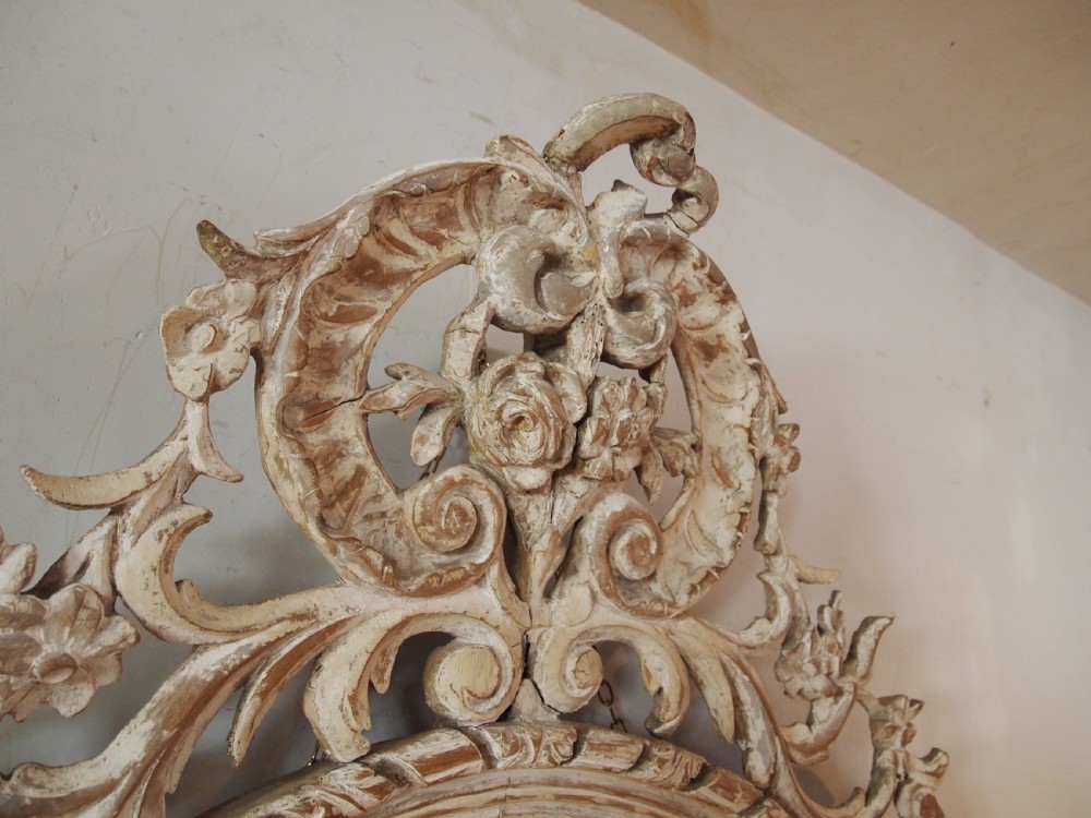 An 18th-century oval wall mirror featuring a heavily carved off-white wooden frame with acanthus leaf motifs and an ornate scrollwork cresting. View VII